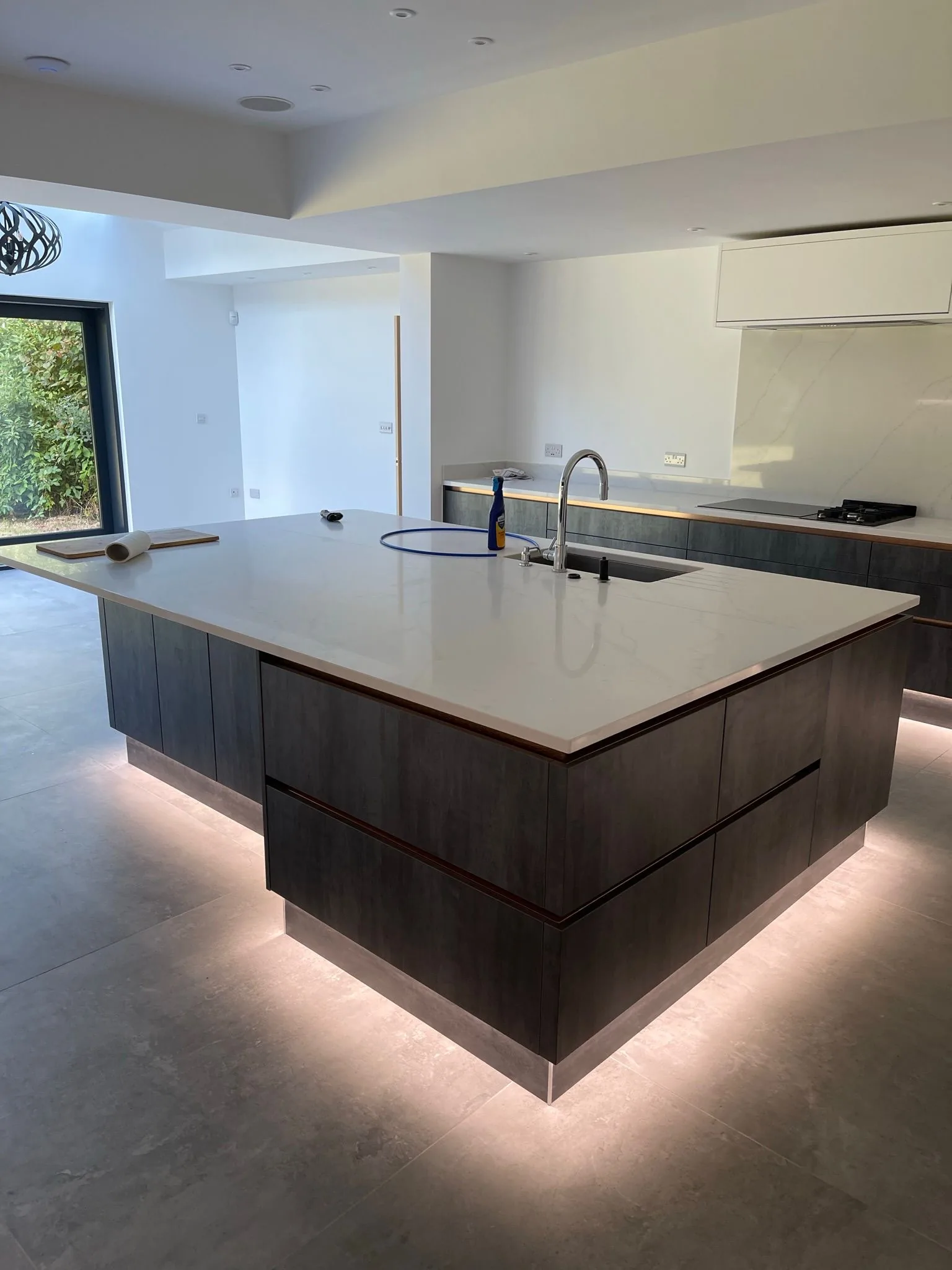Dark handleless fitted kitchen with waterfall-edge island and integrated LED plinth lighting