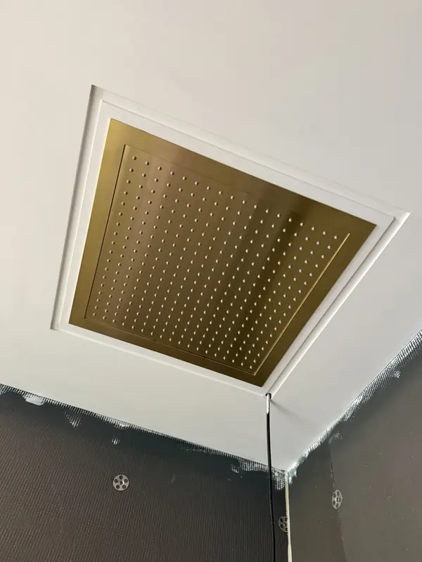 Square brushed brass rain shower set flush into a white ceiling