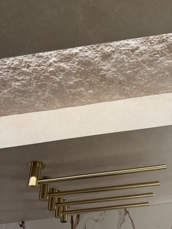 Brushed brass towel warmer bars beneath a textured stone niche