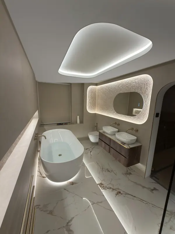 Finished en-suite by Joinery Limited with a lit curved ceiling, freestanding bath and walnut vanity