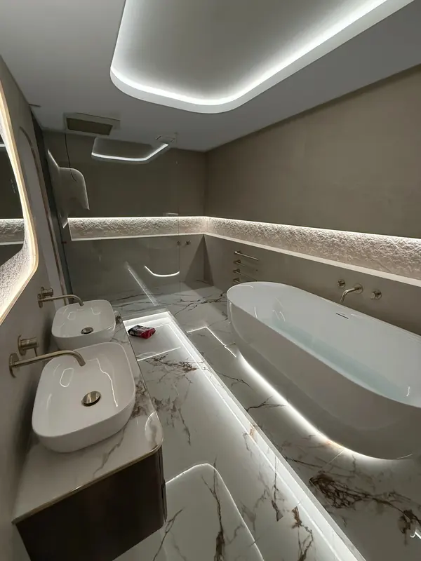 Walnut double vanity with brass taps opposite a freestanding bath and a lit stone niche