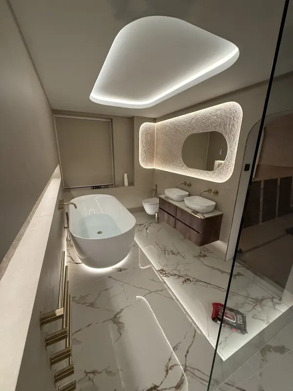 The finished en-suite viewed from the shower, with a lit coffer, bath and vanity