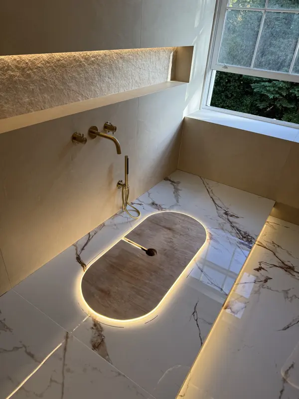 Lit bath plinth with a timber cover beneath a lit stone window niche