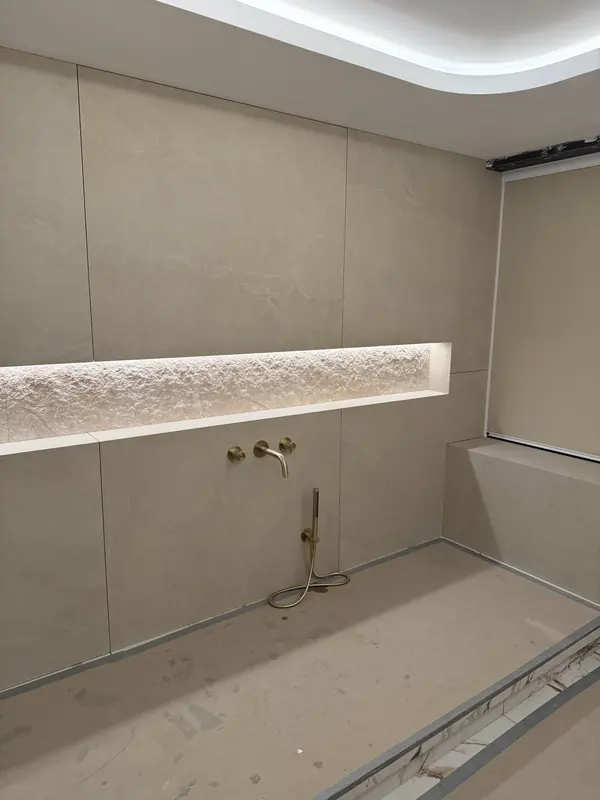 Long lit stone niche above brass shower fittings in a tiled wet room