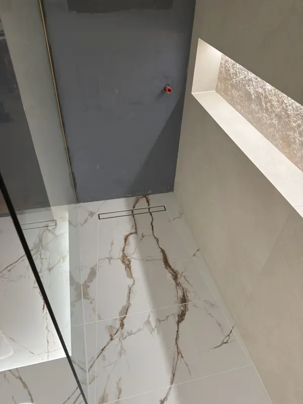 Marble-effect shower floor with a linear drain behind a frameless glass screen