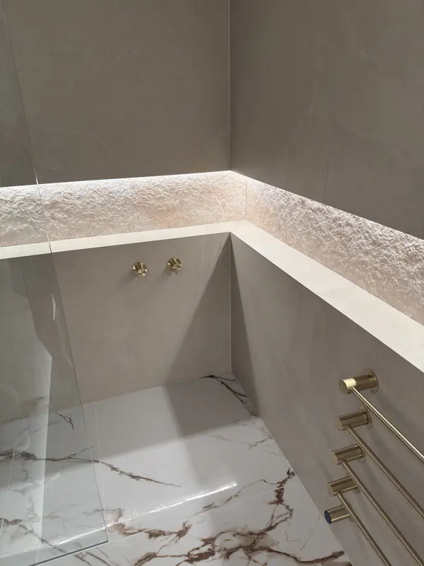 Walk-in shower with brass towel warmers, a lit stone niche and a marble-effect floor