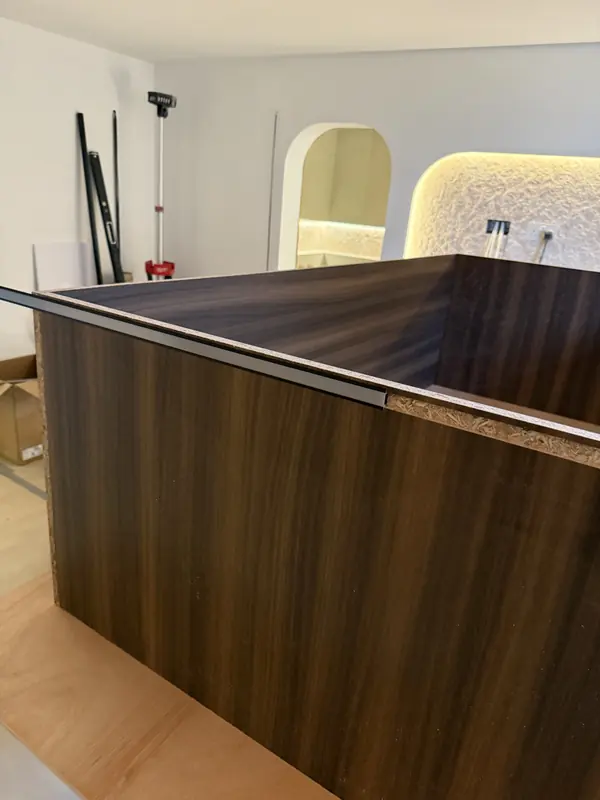 Walnut-veneered carcass with an edge trim being fitted