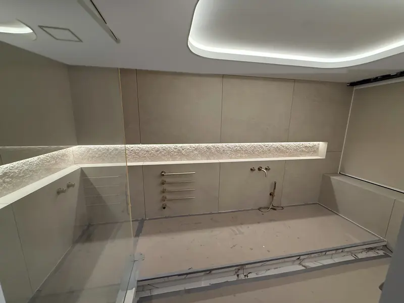 Tiled walk-in shower with a long lit stone niche and brass towel warmers
