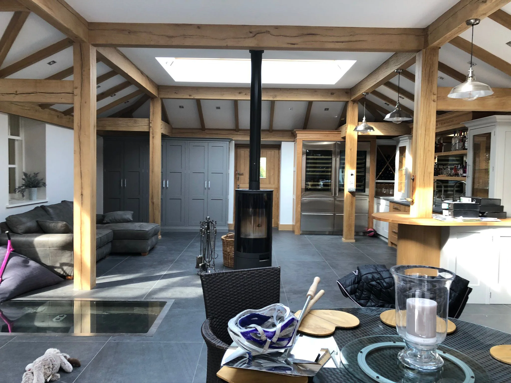 Oak-frame open-plan kitchen and living room with central log burner and grey shaker units