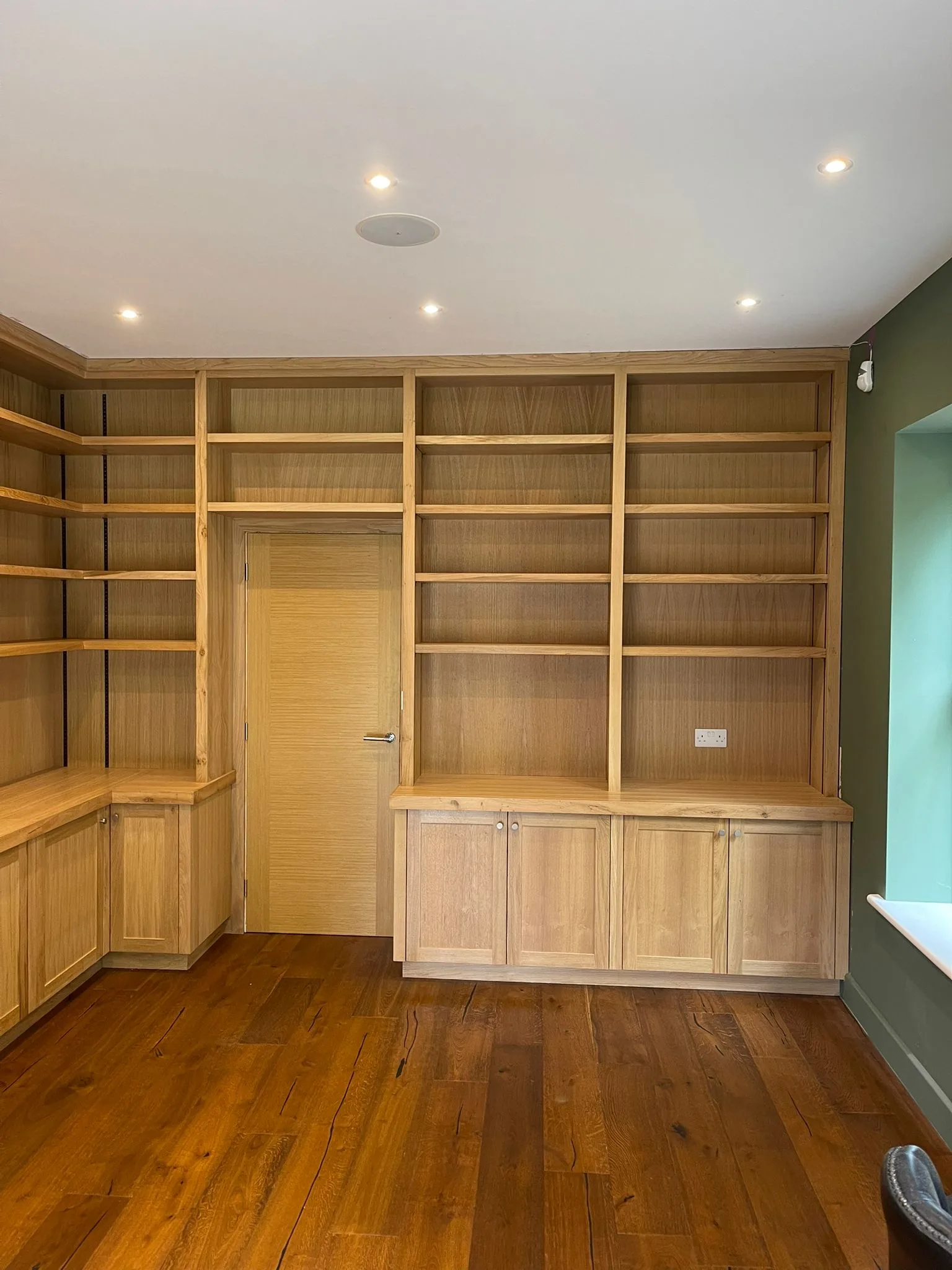 Bespoke oak library with full-height shelving wrapping around a flush door