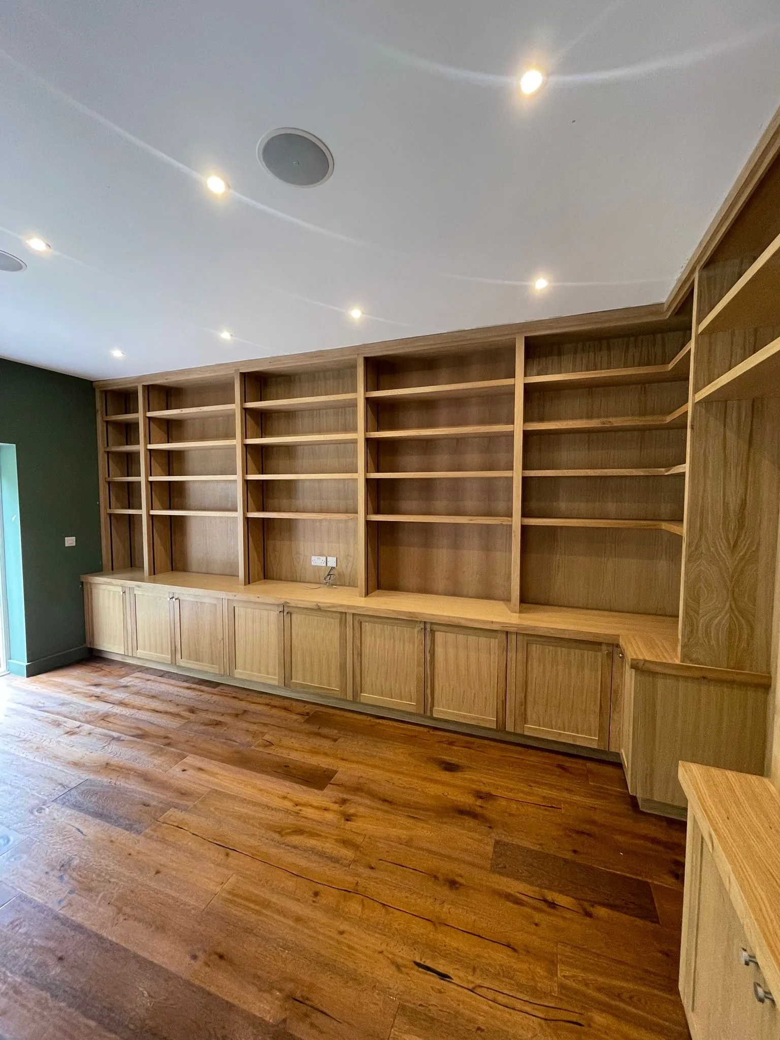 Bespoke oak library wall with five bays of tall open shelving and panelled cupboard doors