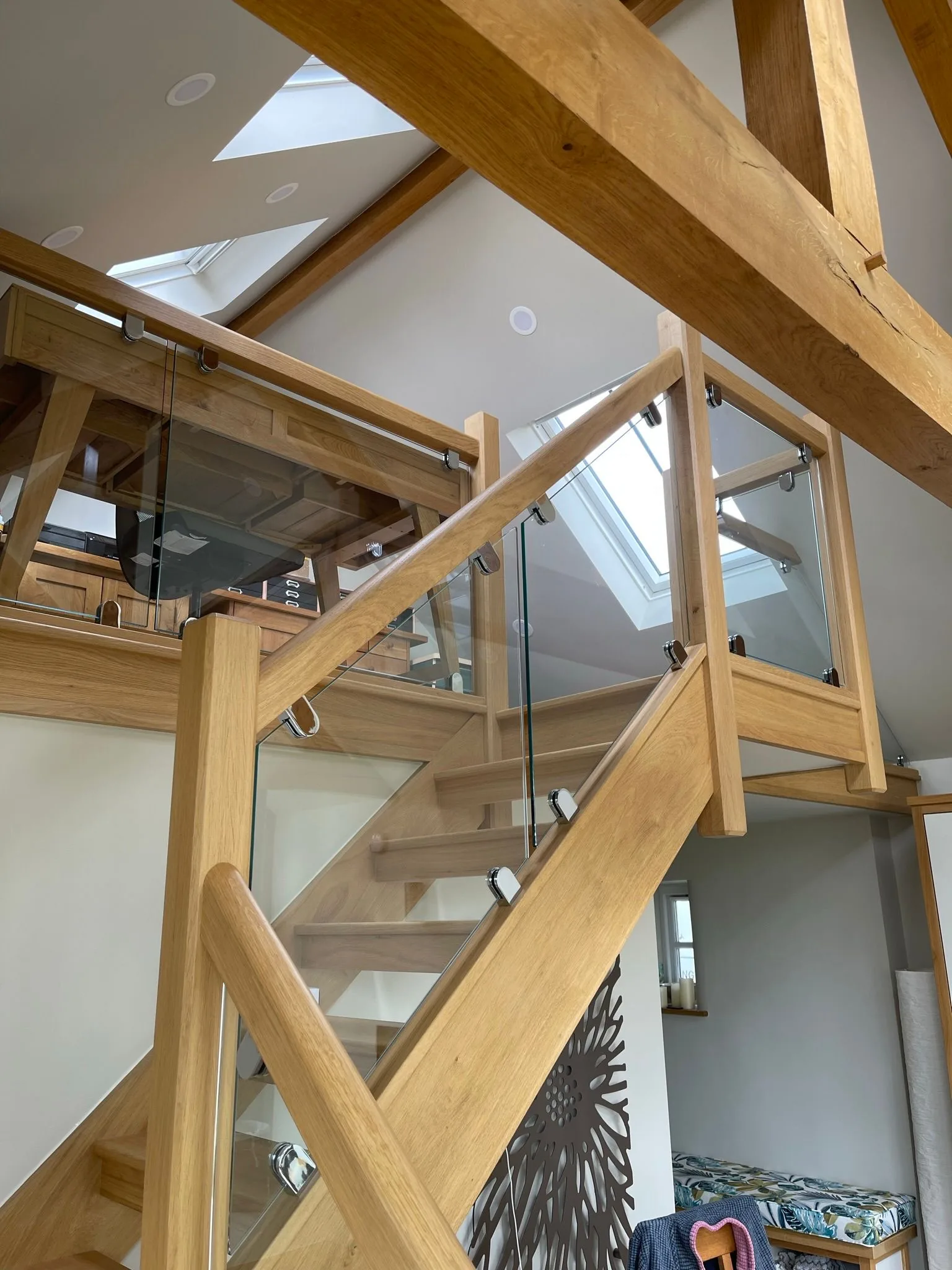 Bespoke oak staircase with frameless glass and exposed oak trusses under a skylight