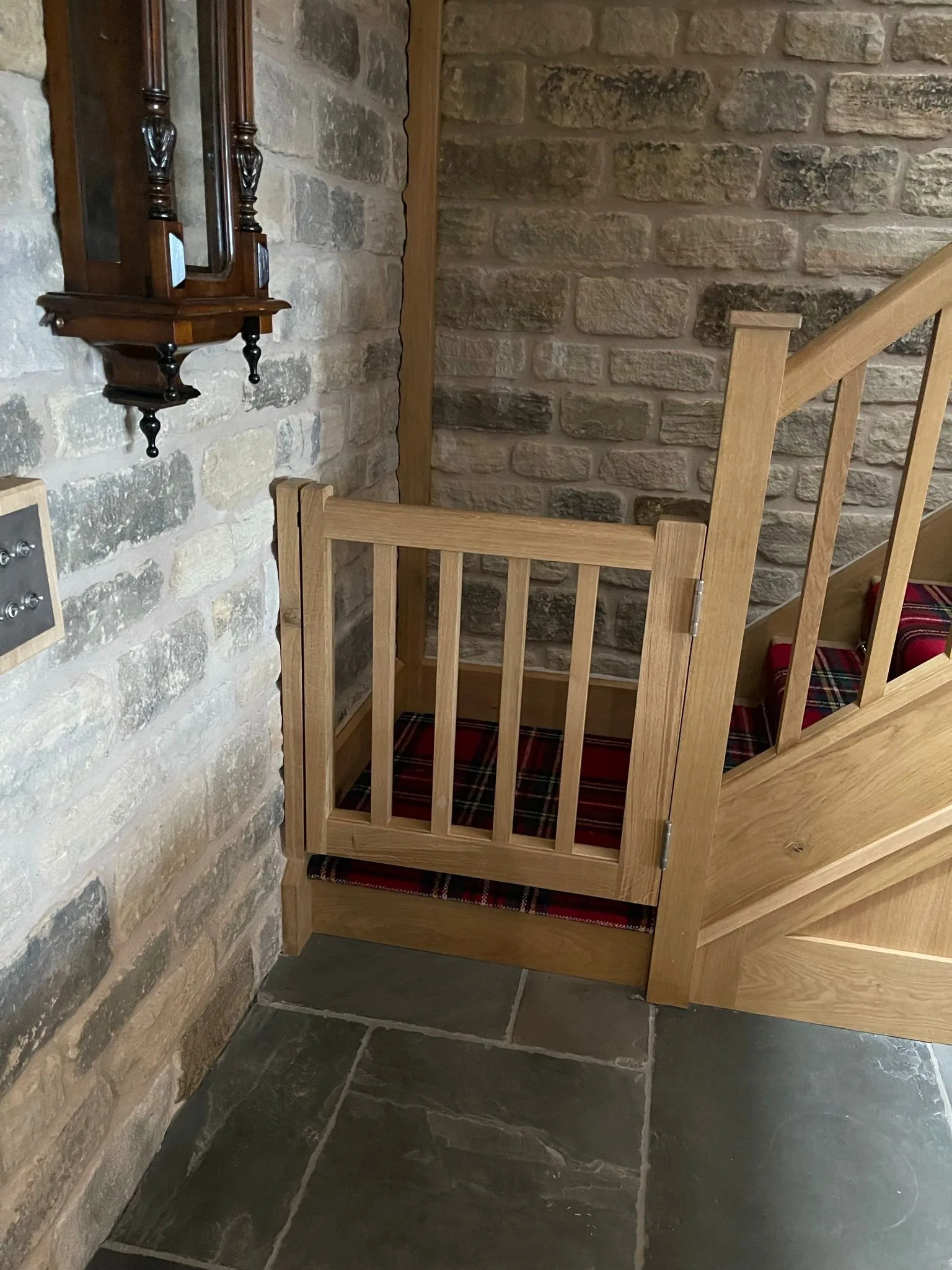 Bespoke oak staircase with safety gate set against an exposed stone wall