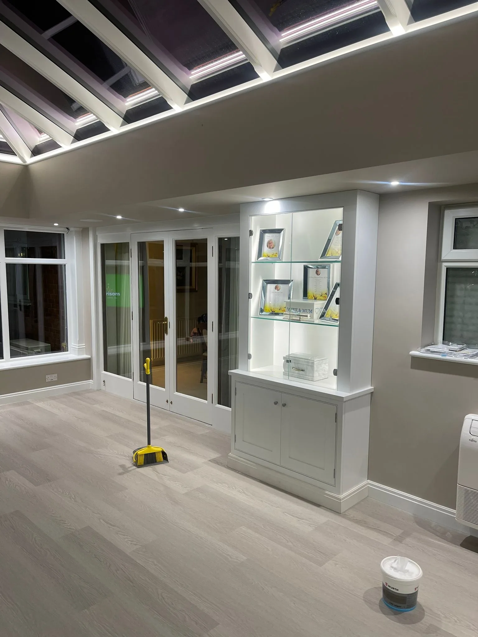 Interior of a painted timber orangery with integrated display cabinetry beneath the full-height glazing