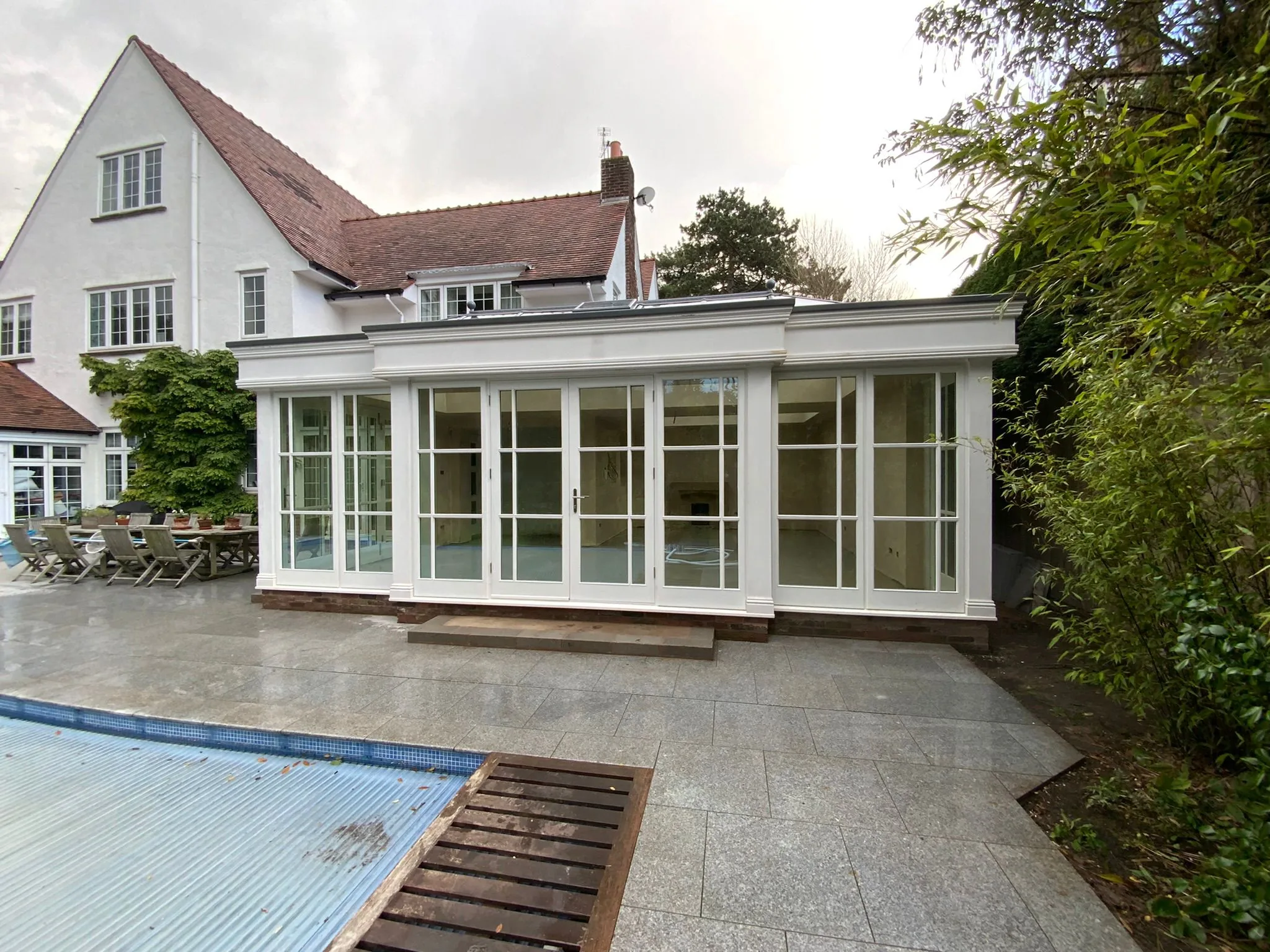 Painted timber orangery with Georgian-bar glazing overlooking a granite pool terrace