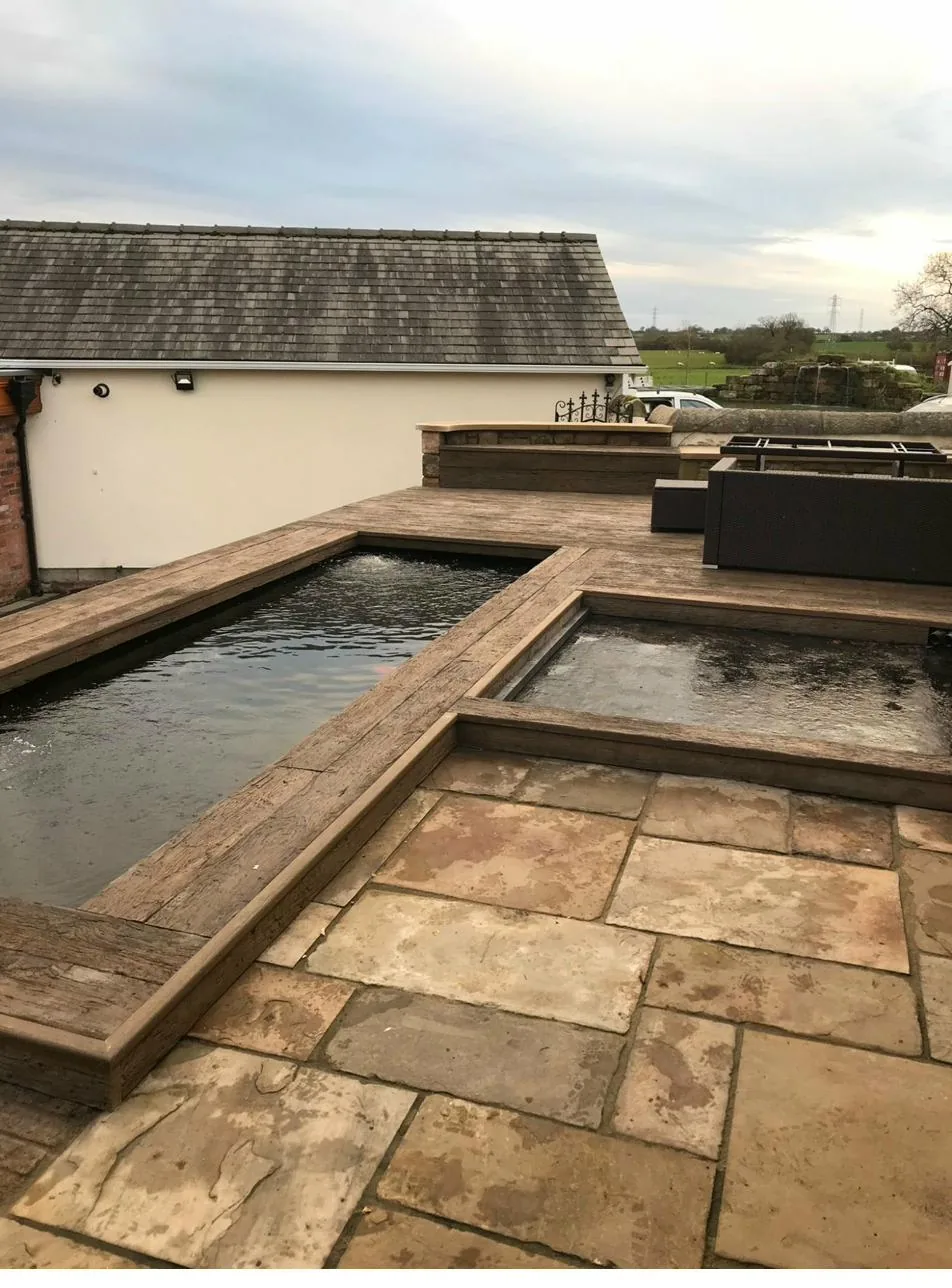 Bespoke outdoor sunken pond with sandstone paving and timber sleeper edging